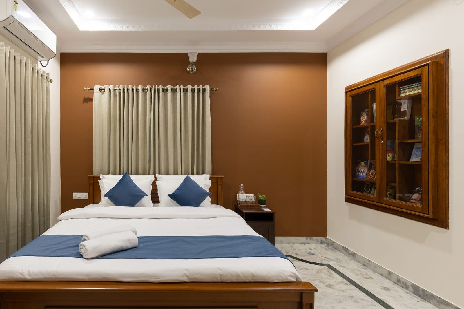 Room 1 from the foot of the bed, with the glass display cabinet and the curtained window