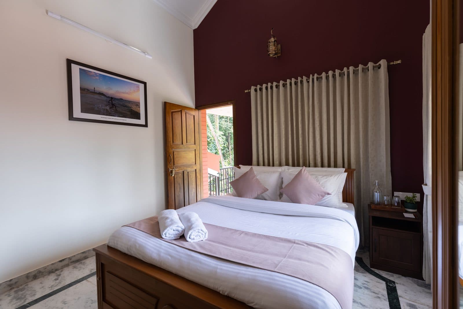 Room 3: a queen bed against a maroon wall, with the door to the balcony open