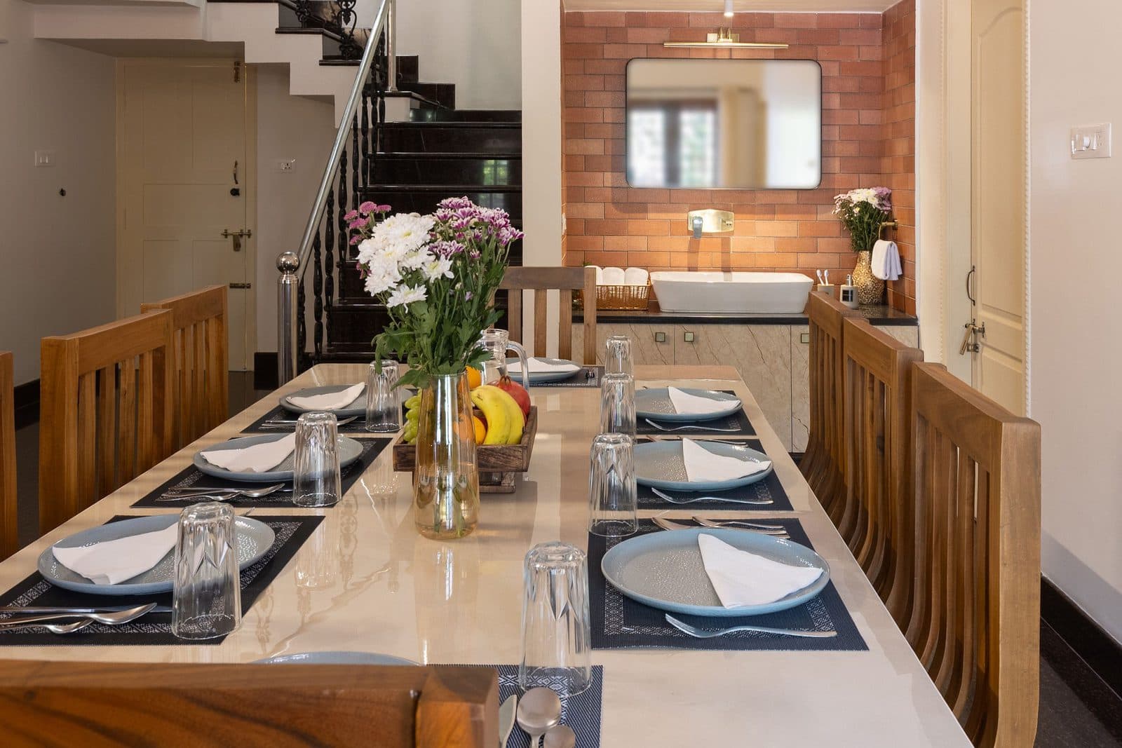 The dining table along the room, with the wash basin and mirror in the brick alcove beside it