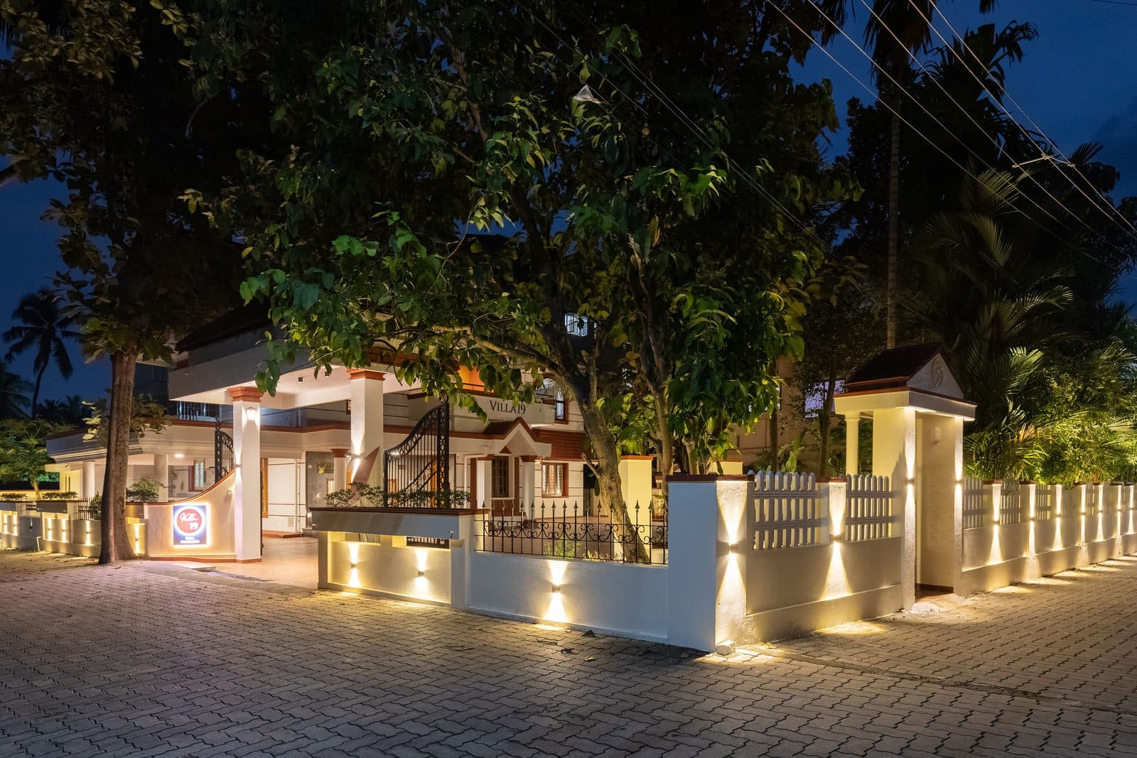 The villa at night from outside the compound, with the lit boundary wall along the road