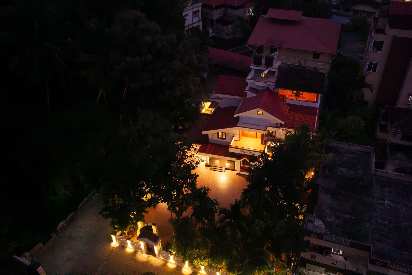 The villa from above after dark, lit from inside, with lamps along the compound wall