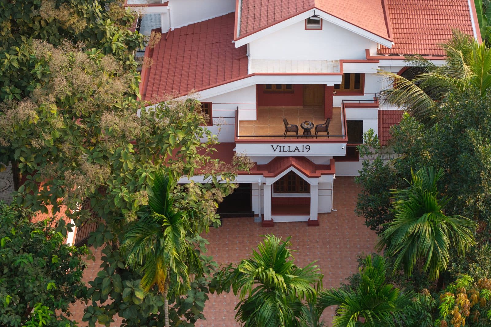 The villa from above, with the first-floor sit-out, the tiled roof and the trees around the compound