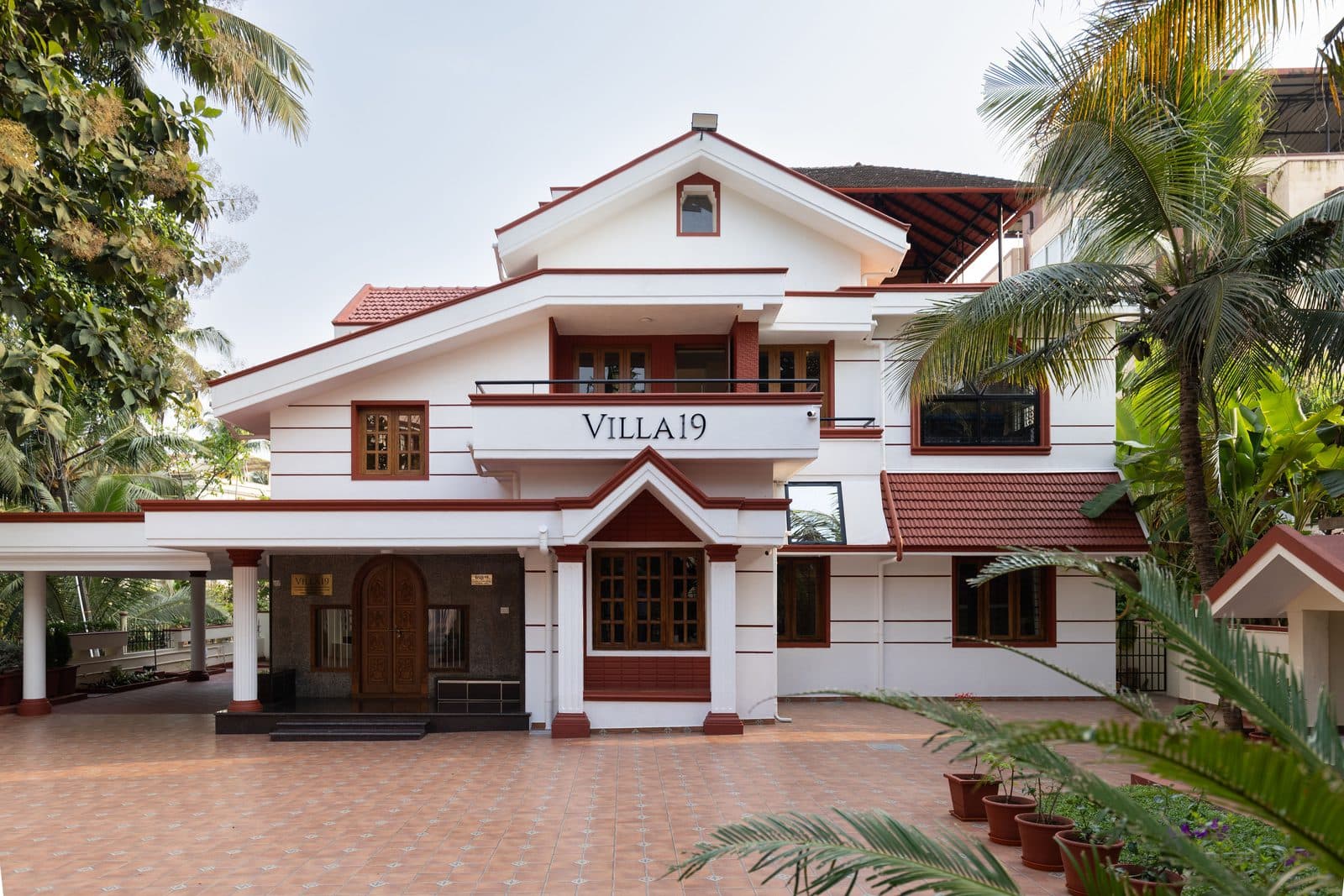 The front of the villa in daylight, with the Villa 19 name on the first-floor balcony and palms on either side